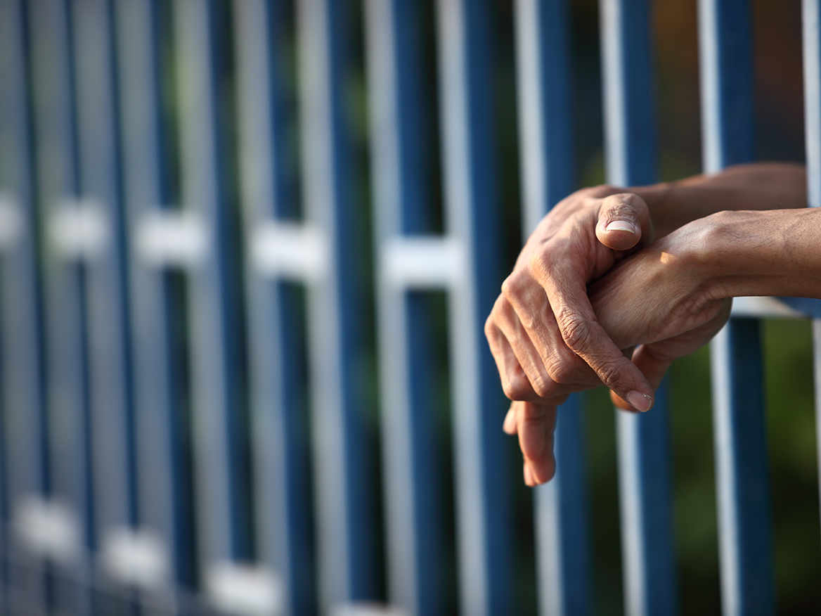 Crossed hands hanging across prison bars.