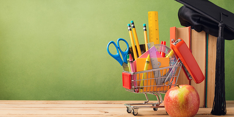 School supplies in a miniature shopping cart near an apple and three books that students can choose to buy with their education credit.